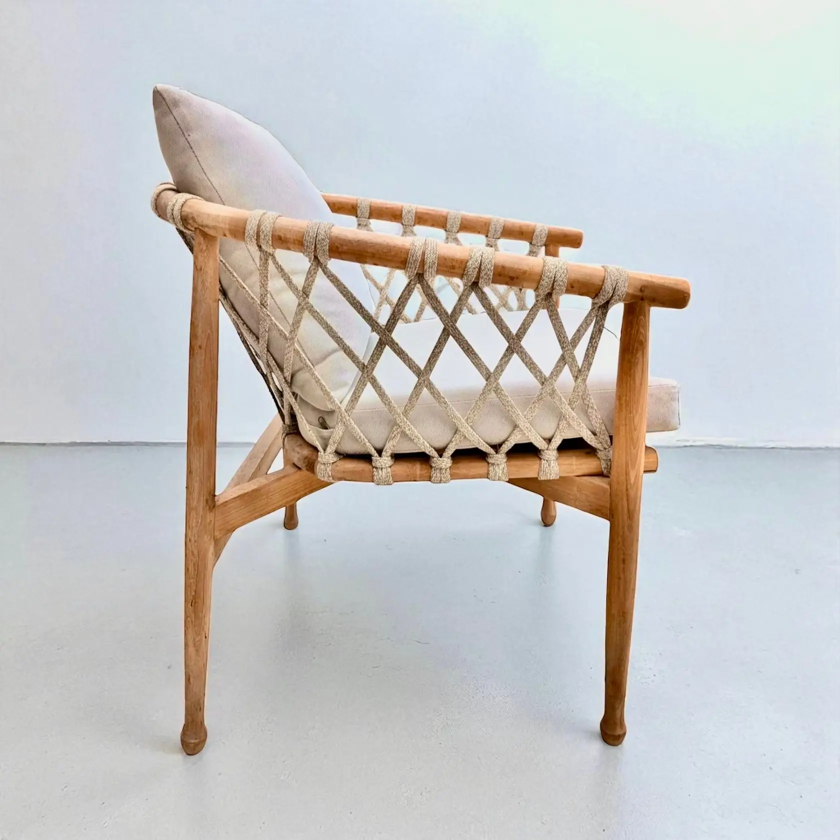 Fauteuil Bintang en teck massif clair, cadre en rondins, flancs en lanière écrue croisée, coussins écrus