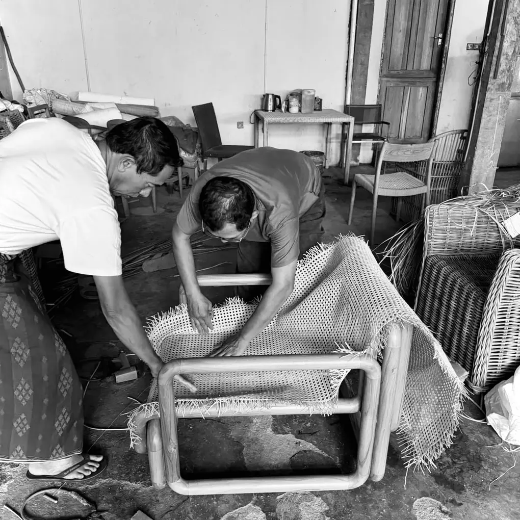 At the workshop in Indonesia: two craftsmen fitting rattan cane to a teak lounge chair